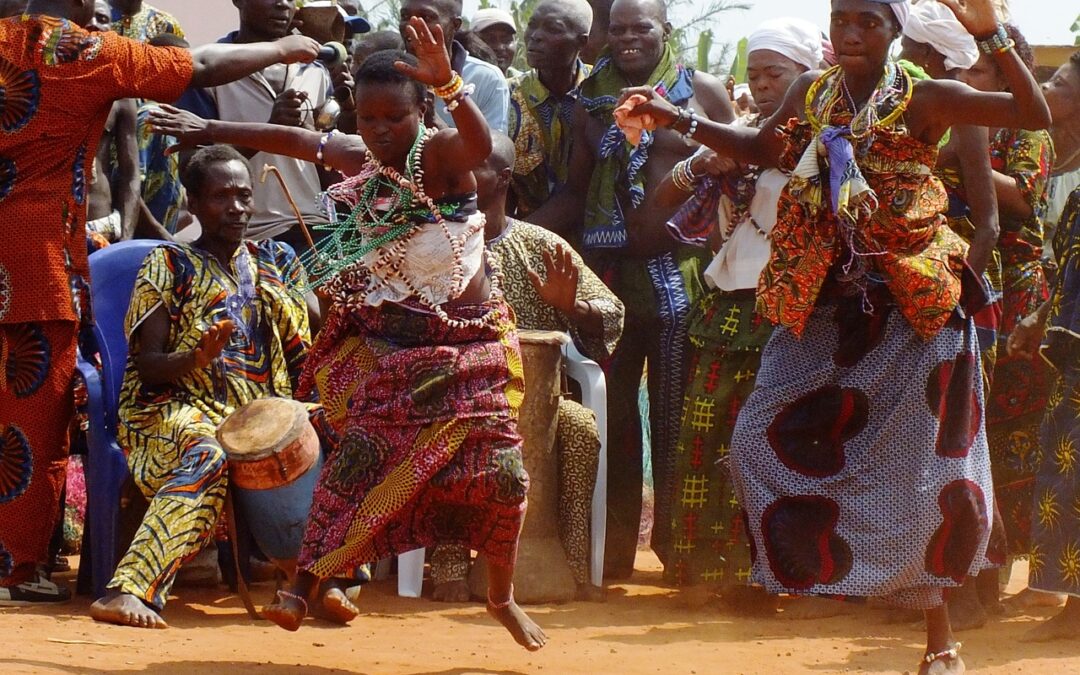 Een groep mensen voert een voodoo ritueel uit in een Afrikaans dorp. Ze dansen en zingen rond een altaar met kaarsen en offergaven, terwijl een priester de ceremonie leidt.